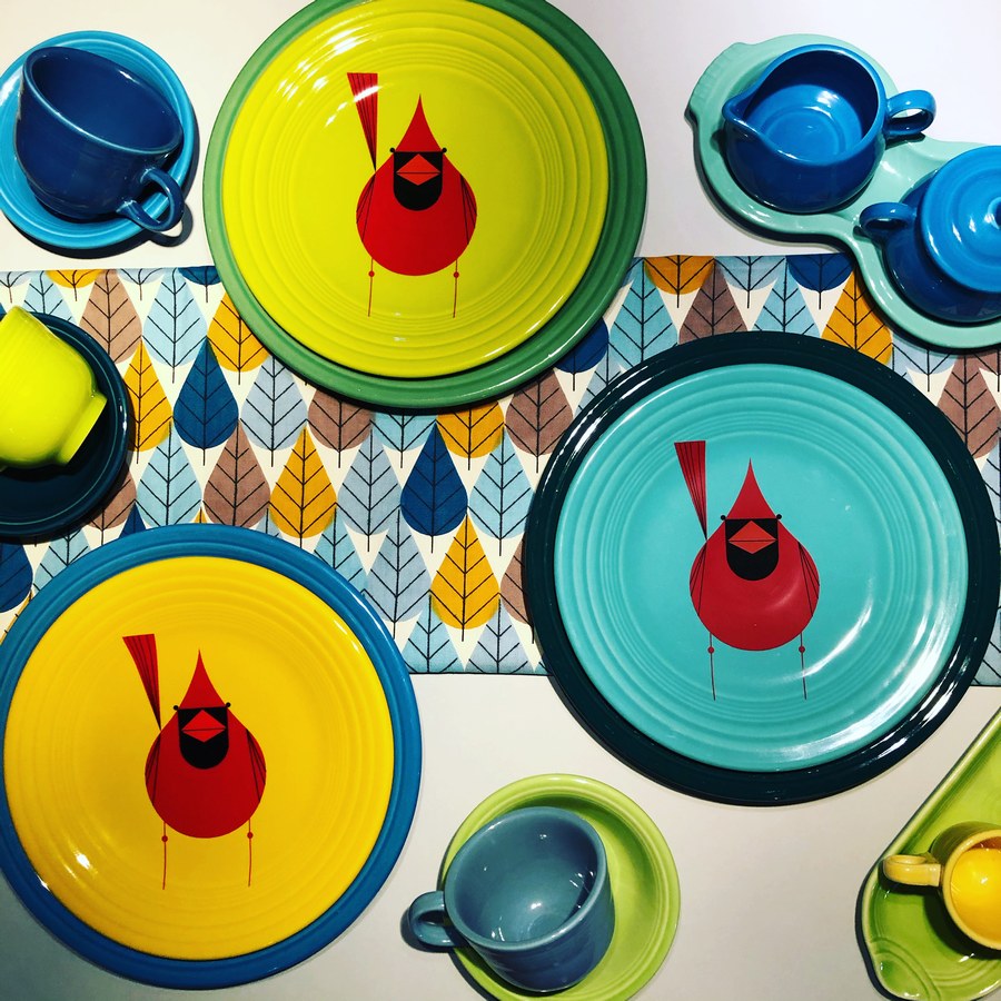Fiesta plates arranged with a strip of Octoberama Blue fabric on a white background, with several brightly colored mugs and saucers nearby